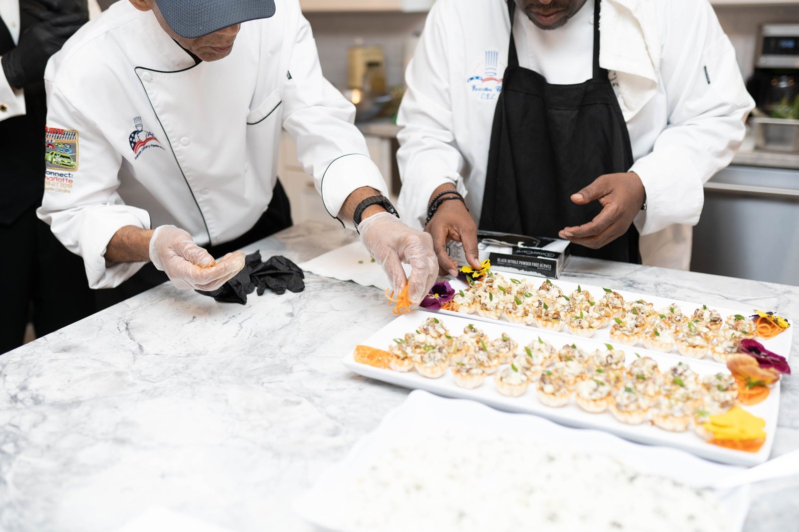 Two chefs garnishing trays of tartlet canapés