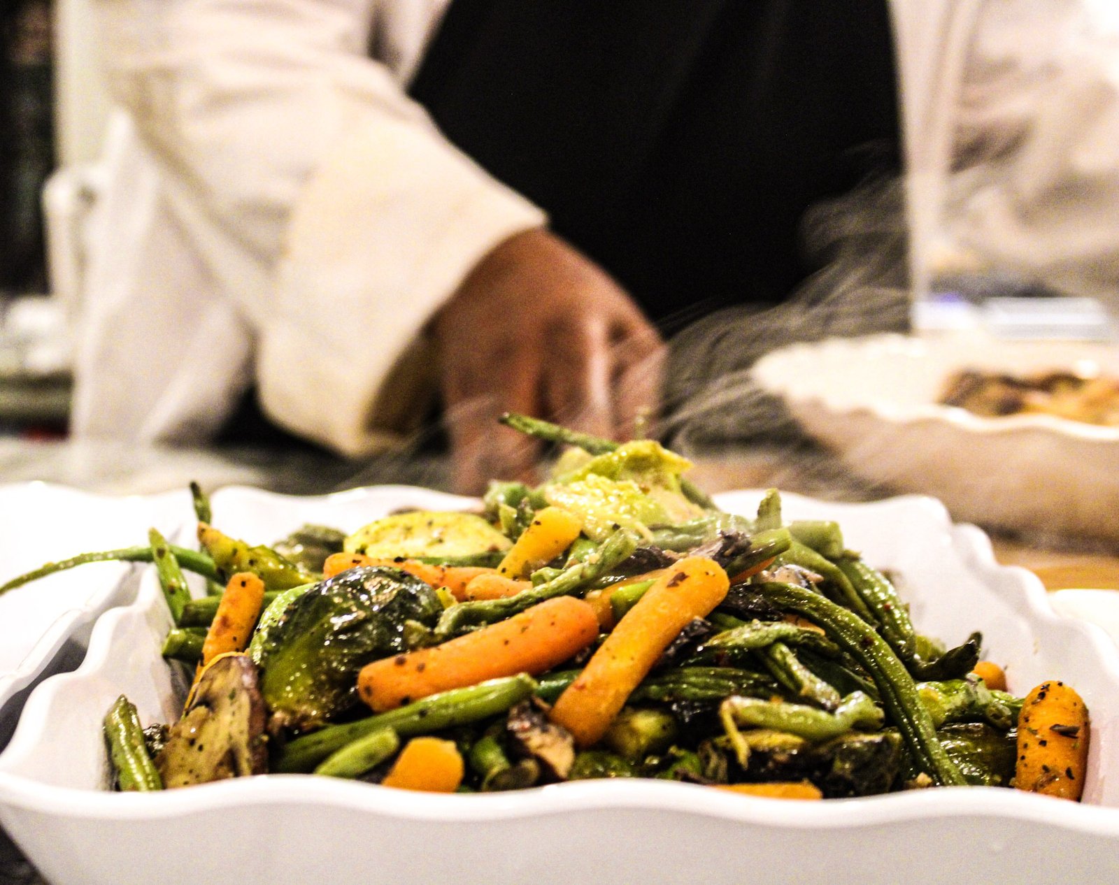 Roasted vegetables on a tray, a chef working in the background